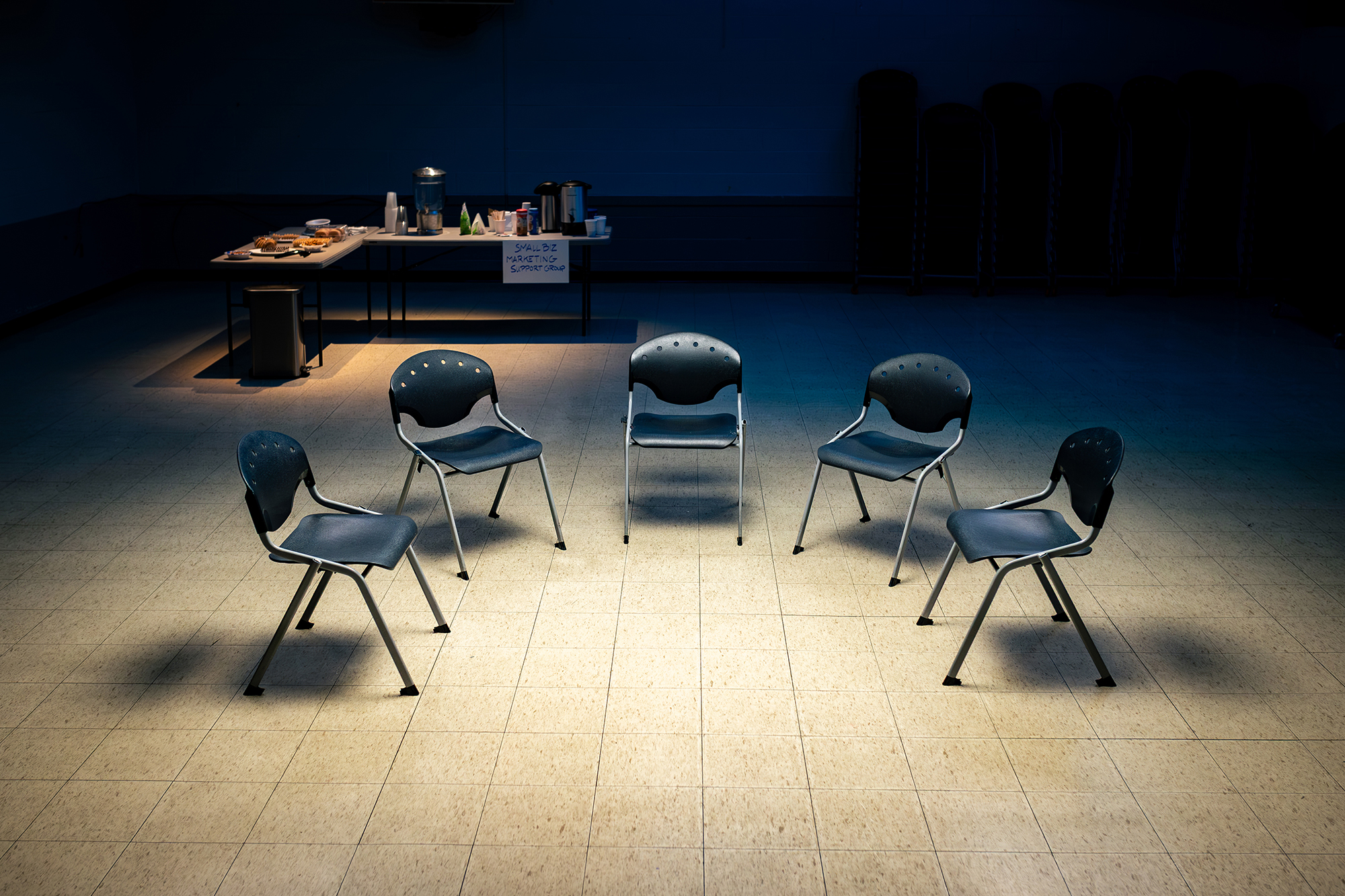 Empty chairs arranged in a circle in a dimly lit room — the support group before Levitate